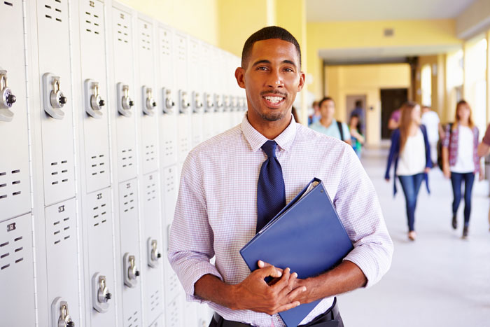 A picture of a smiling teacher standing by a row of lockers in a school hallway.