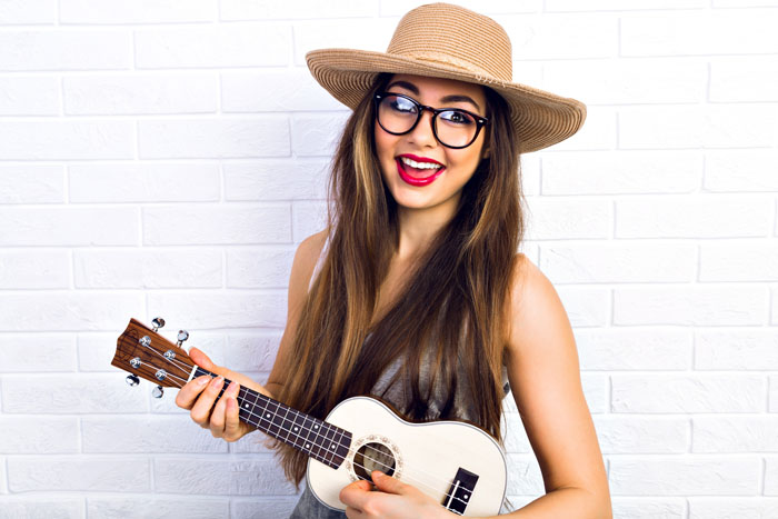 A picture of a smiling young woman playing the ukulele.